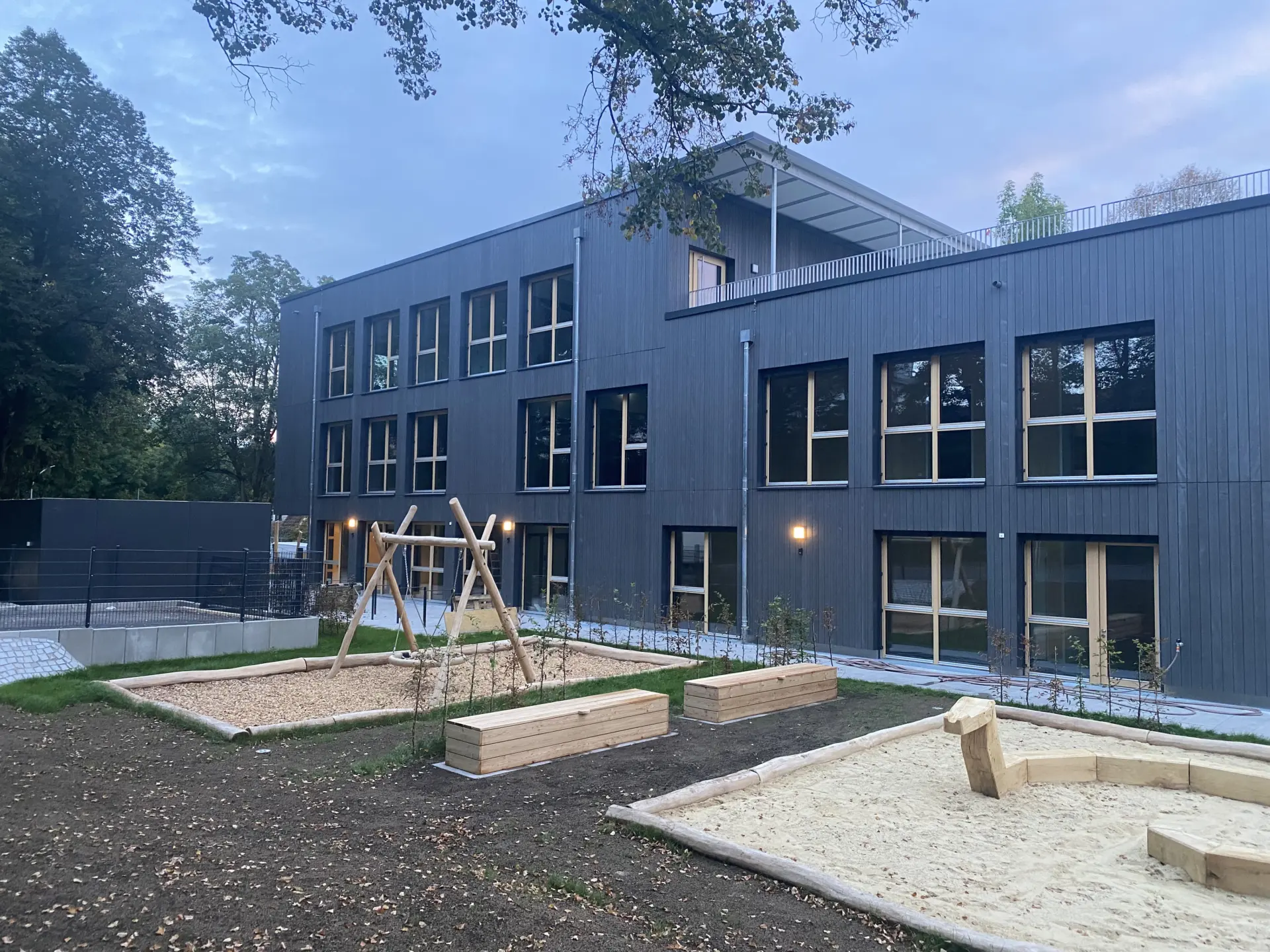 Gartenansicht Kindertagesstätte Manzen – Sandkasten und Spielbereich vor dreigeschossigem Holzbau, Hagedorn Ingenieure Göppingen