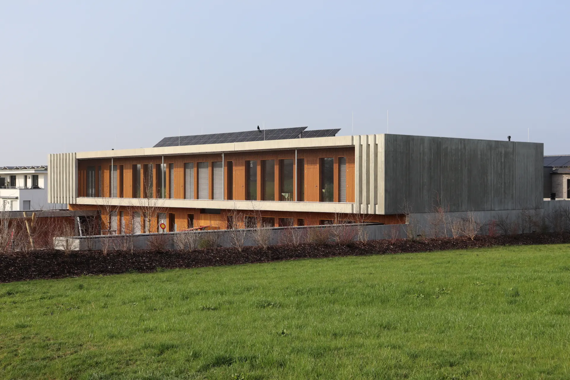 Zweigeschossiger Neubau mit Sichtbeton und Holzlamellen-Fassade in Grünanlage