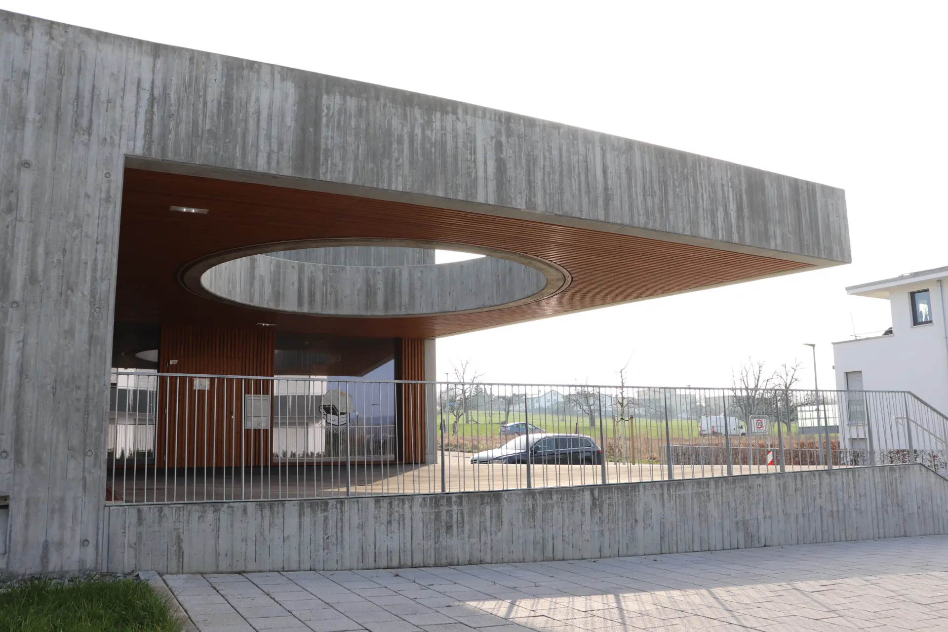 Detailansicht des auskragenden Sichtbeton-Vordachs mit ovaler Öffnung und Holzlamellen